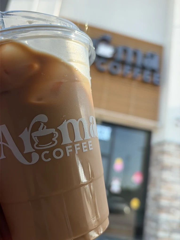 Iced Aroma Coffee cup held in front of the shop